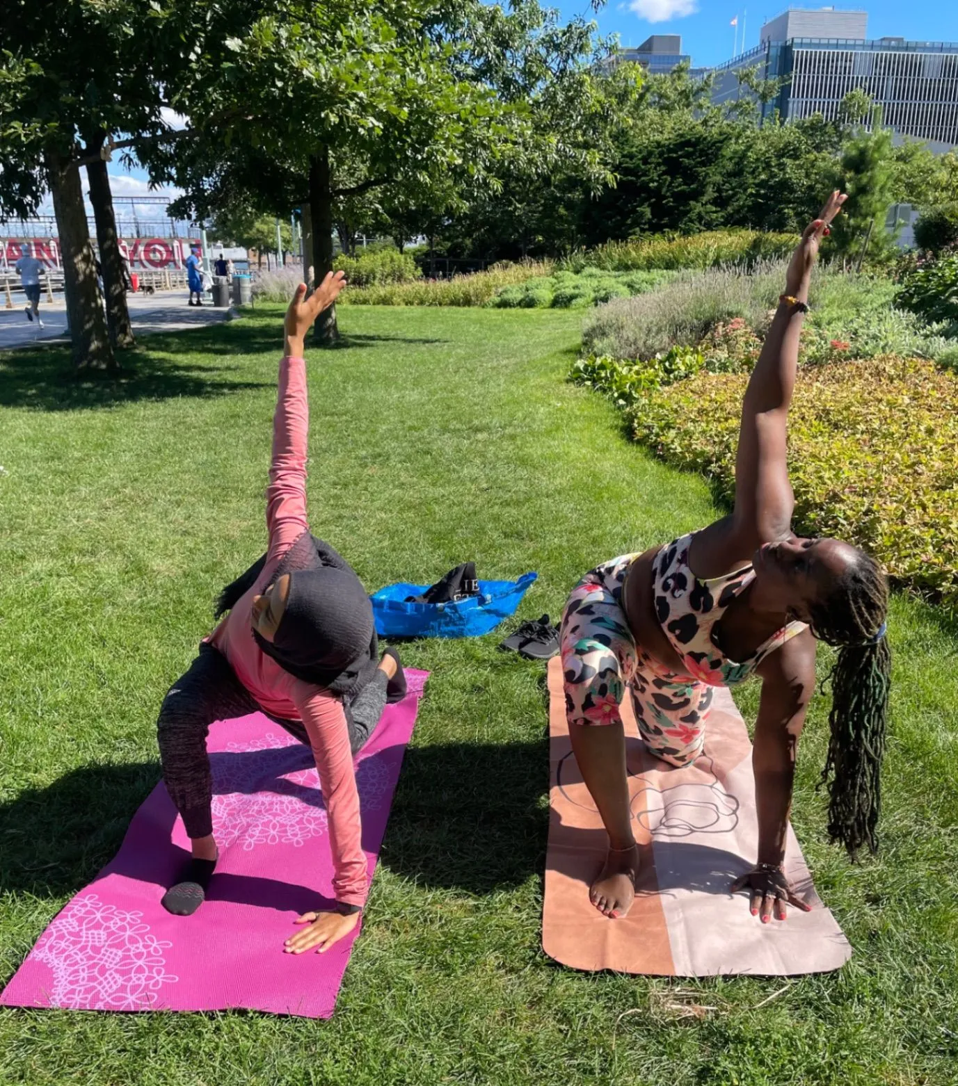 Two women practicing yoga outdoors on colorful mats in a sunny garden